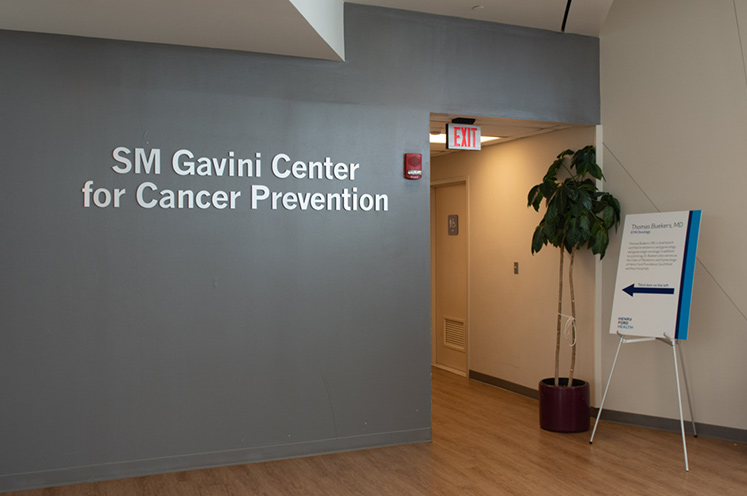 Hospital waiting room with medium hardwood floors and gray accent wall with sign saying, “SM Gavini Center for Cancer Prevention”.