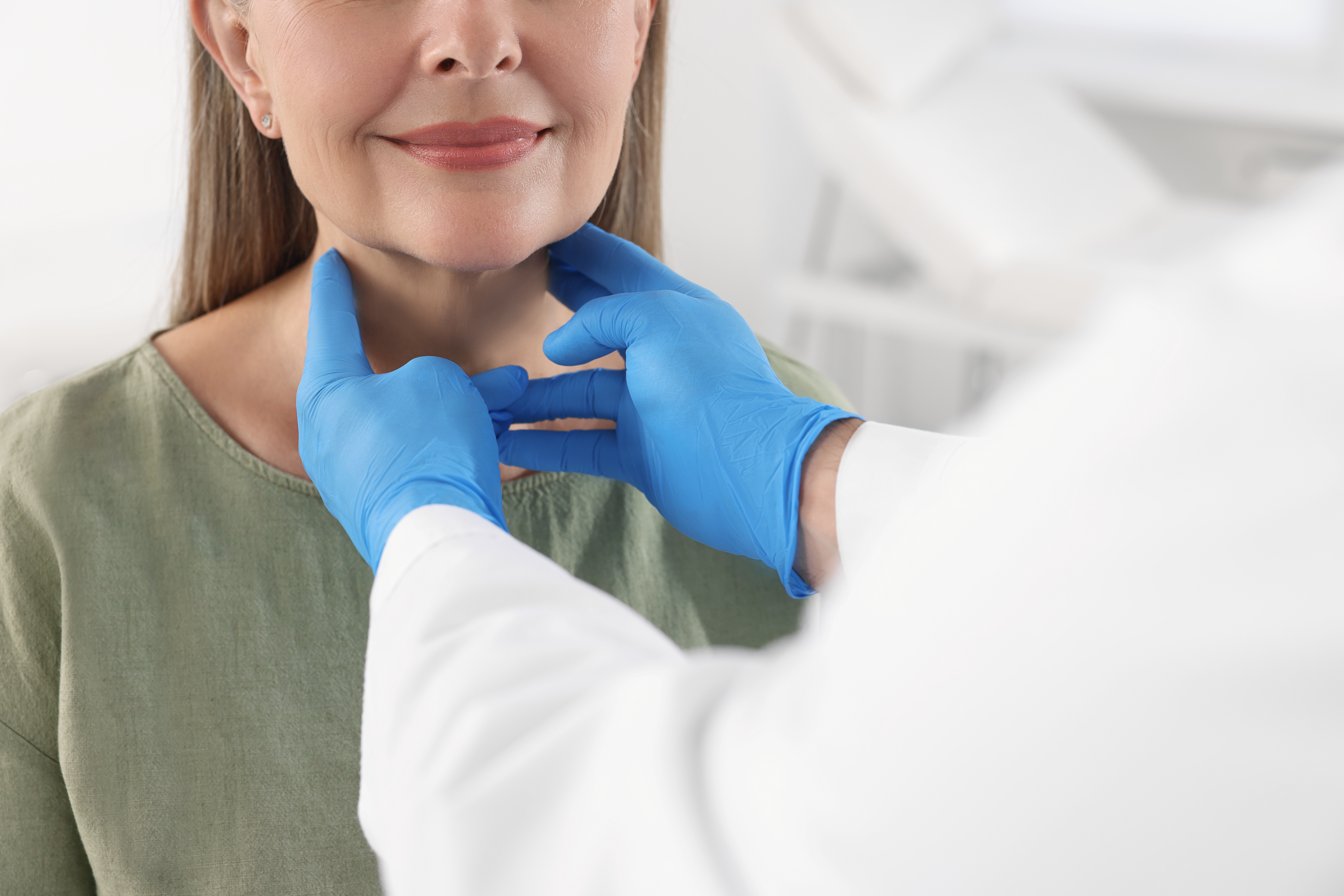 Clinician wearing blue medical gloves examines a woman’s neck during an endocrinology evaluation at Henry Ford Health. 