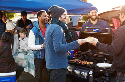 A group of people standing around a bar-b-que grill talking