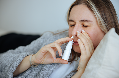 sick woman using nasal decongestant spray