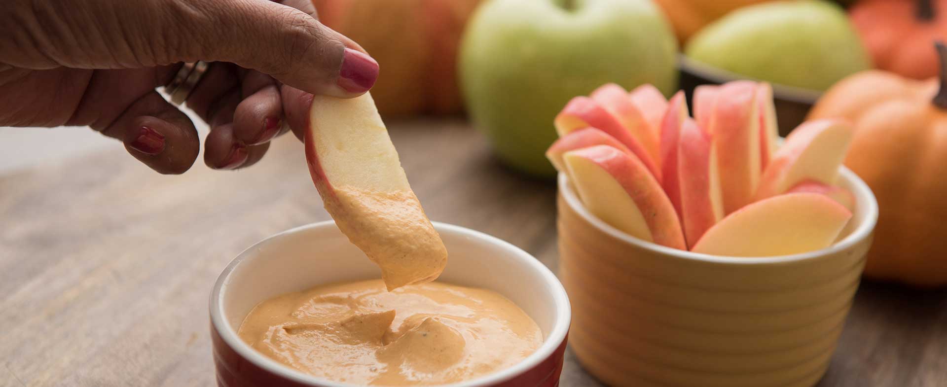 Hand scooping creamy pumpkin dip with an apple slice
