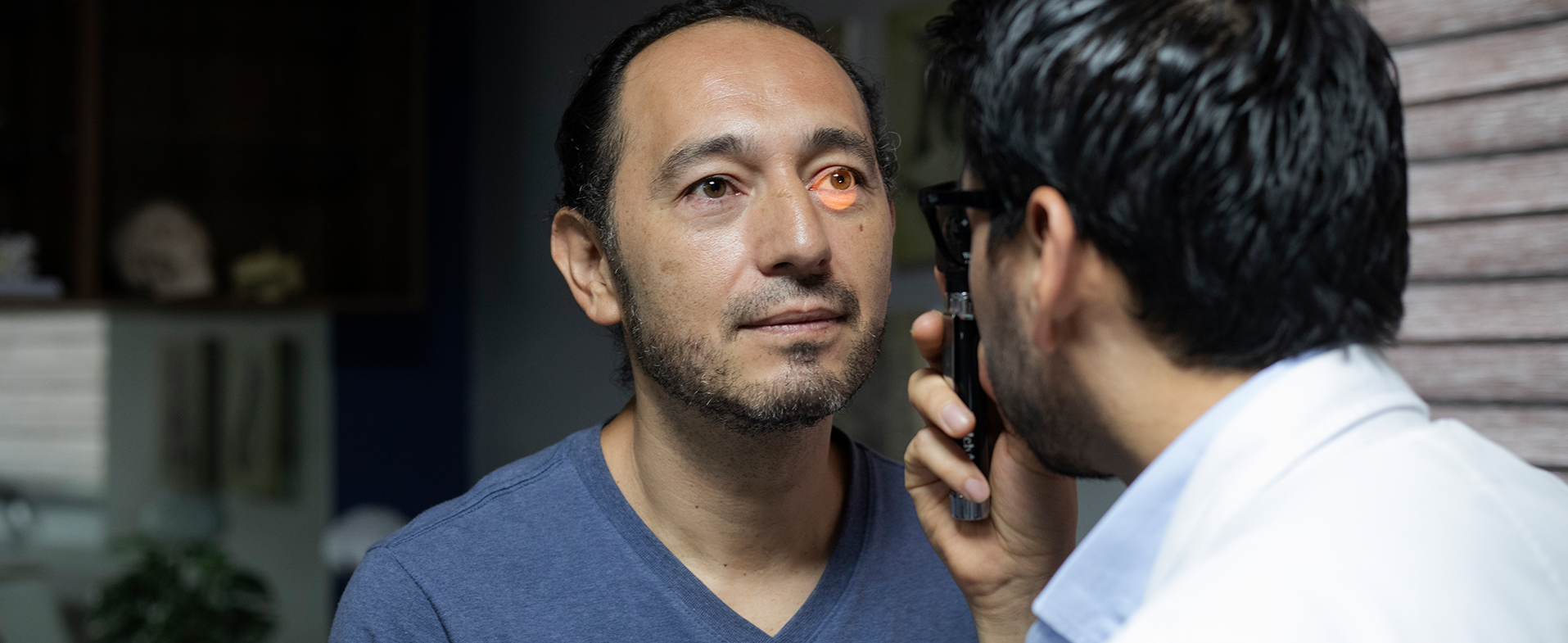 Man wearing a blue v-neck t-shirt and getting his eyes checked. man getting vision checked