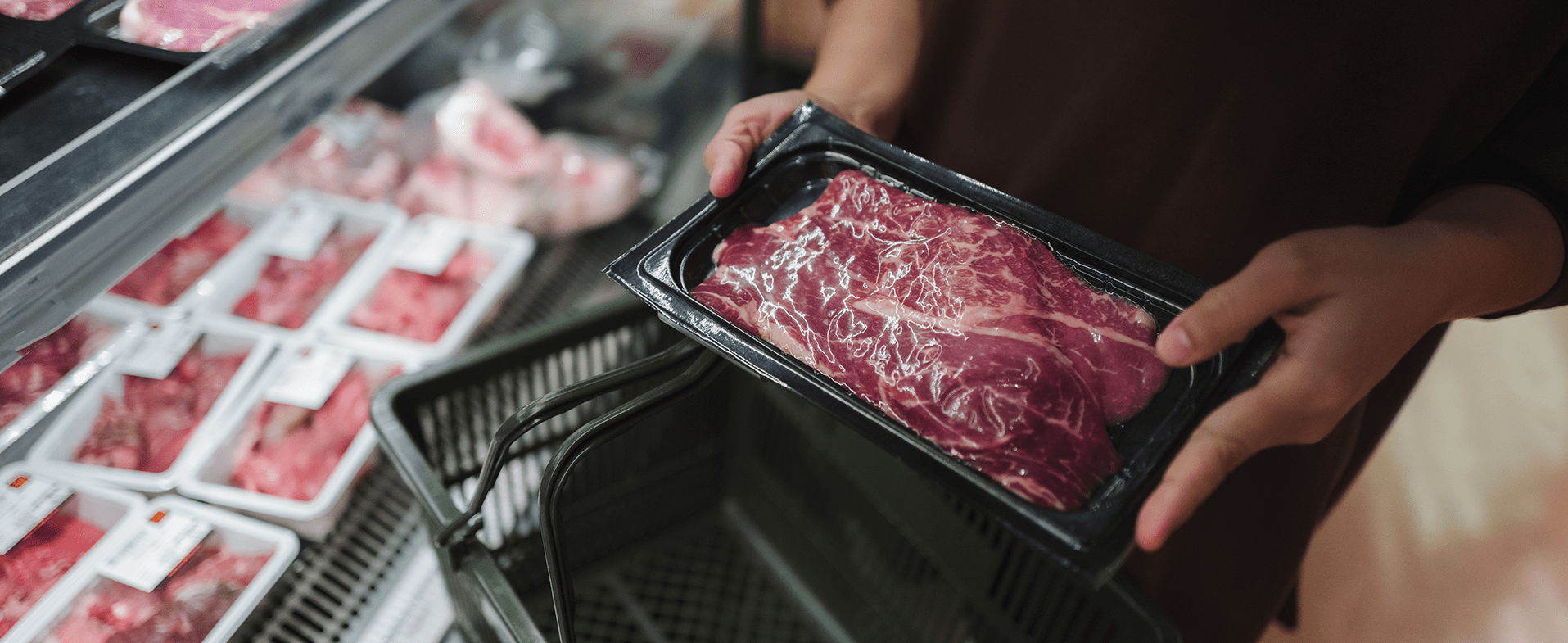 Close-up of someone putting red meat in a shopping cart at the grocery store. dummy desktop Image