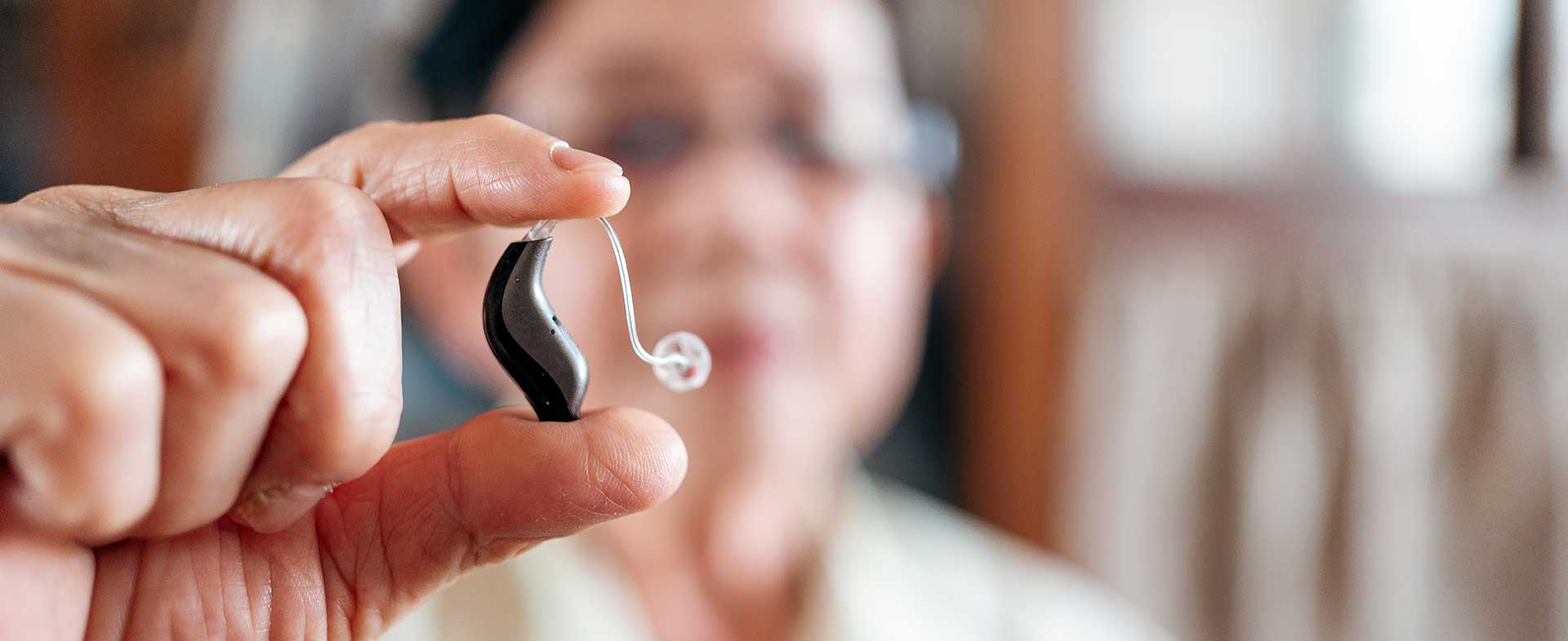 A person holds a hearing aid up close, with a blurred background. hearing health and dementia