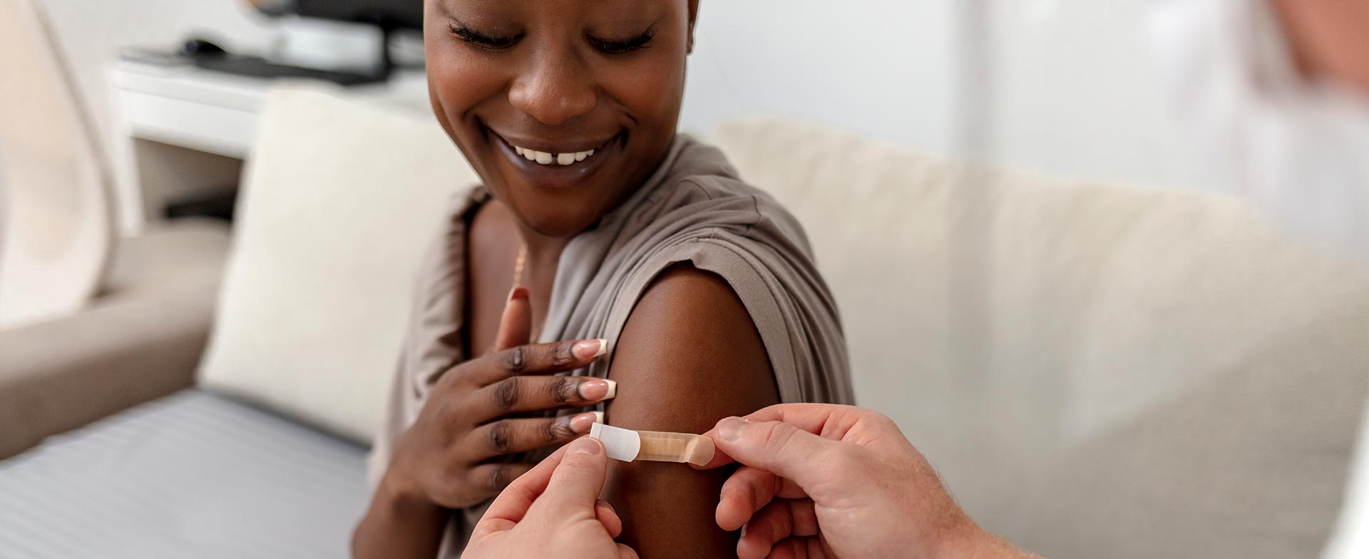 A woman sits smiling with her arm exposed while a doctor puts a bandage on the spot where she just received a shot. adult vaccination catch up schedule