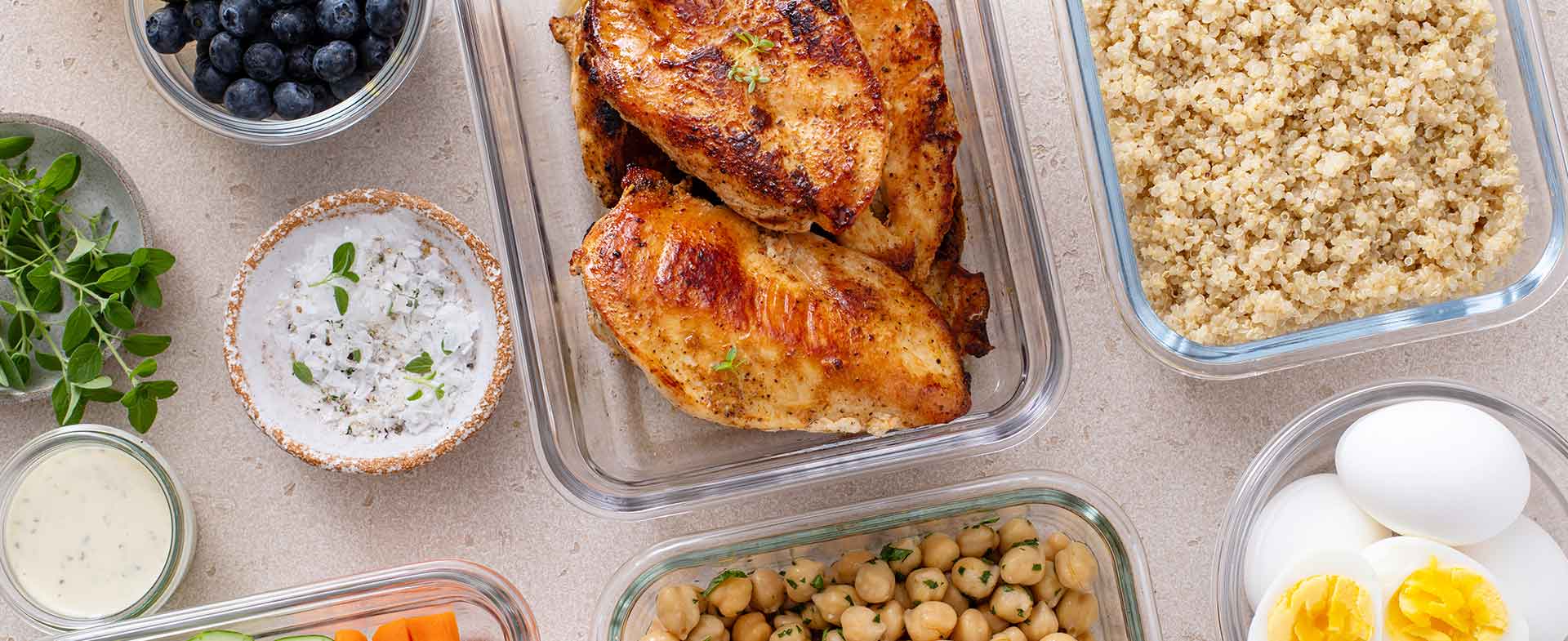 A spread of healthy foods in leftover containers including chicken, quinoa, hard-boiled eggs and chickpeas. high protein meals