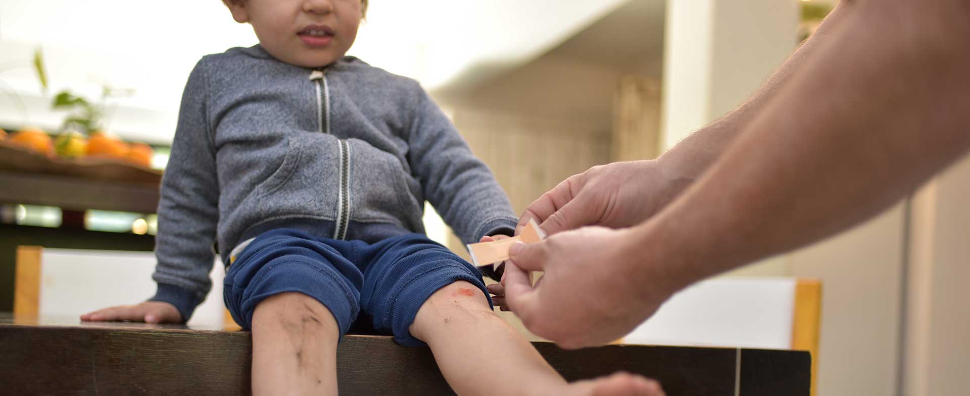 A little boy sits on the counter while his father puts a bandage on his scraped knee. treating minor wounds