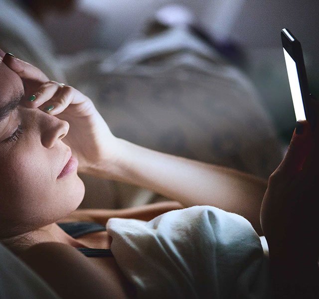 woman in bed looking at a cell phone