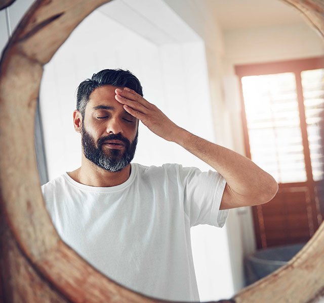 man looking in mirror rubbing forehead