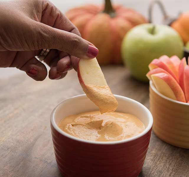 Hand scooping creamy pumpkin dip with an apple slice
