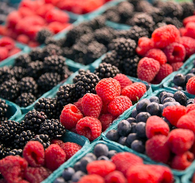 Assortment of fresh berries displayed in light blue cartons. Rows of blackberries, raspberries, and blueberries are visible. berries for fiber