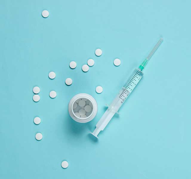A syringe and a small container with scattered white pills are placed on a light blue surface. allergy shots vs meds
