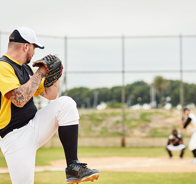Baseball pitcher on mound winding up a pitch. He is wearing a black and white baseball hat, a black and white t-shirt and white baseball pants. He has an arm sleeve of tattoos. dummy mobile image
