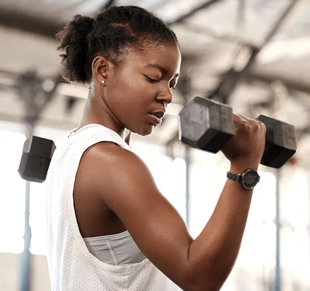 Woman wearing a white tank top with her hair up in a bun and lifting weights. dummy mobile image