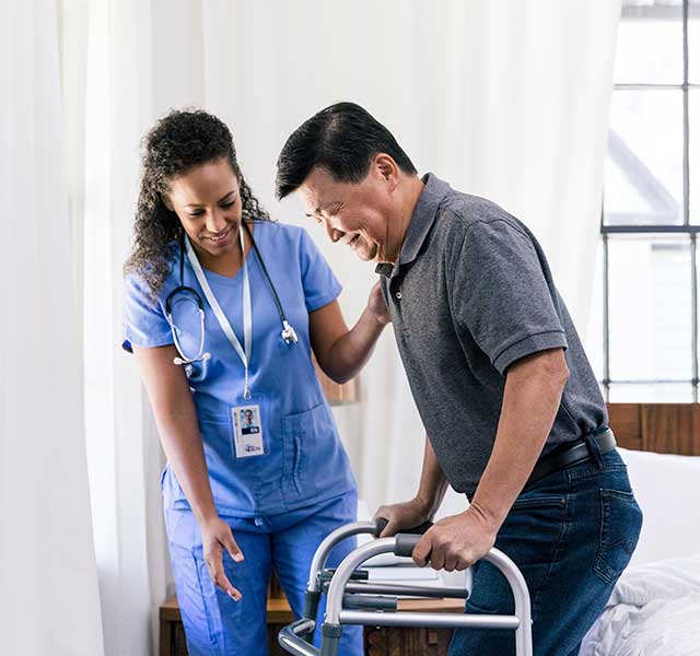A female nurse observes as a male patient stands up from bed with the help of a walker. inpatient stroke rehab