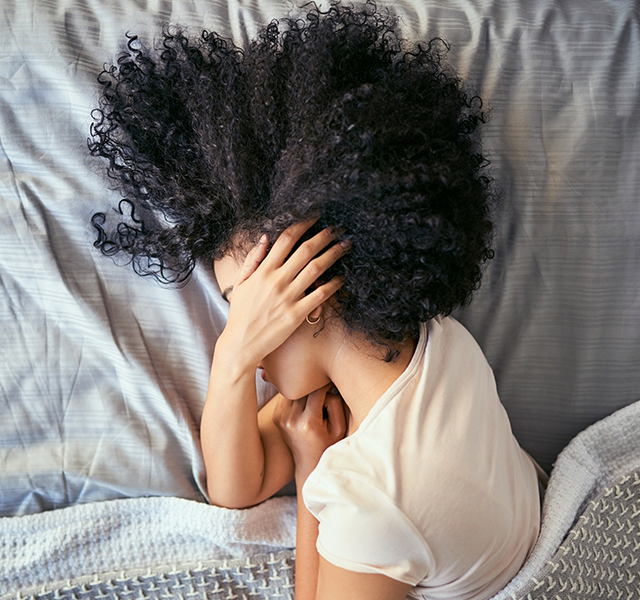 Woman with dark curly hair laying in bed with hand over her ear. dummy mobile image