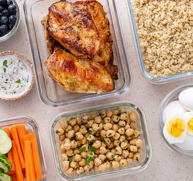 A spread of healthy foods in leftover containers including chicken, quinoa, hard-boiled eggs and chickpeas. high protein meals