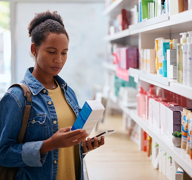 Middle-aged woman in a pharmacy looking at supplements. She has her hair in a high bun and is wearing a denim jacket with a yellow T-shirt underneath. dummy mobile image