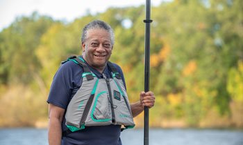 Prostate cancer patient, Donnell, wearing a life-vest and holding a paddle near a lake