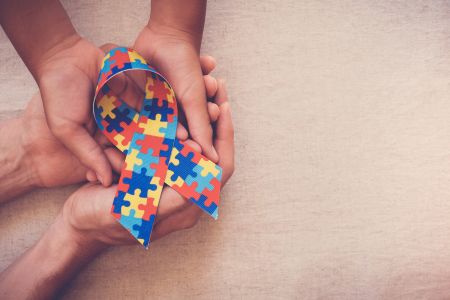 A child and adult join hands to hold a puzzle ribbon for autism awareness at the Henry Ford Health GROW Center for Autism and Intellectual and Developmental Disabilities.