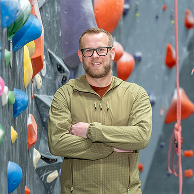 vascular surgery patient Eric posed in front of a rock climbing wall indoors