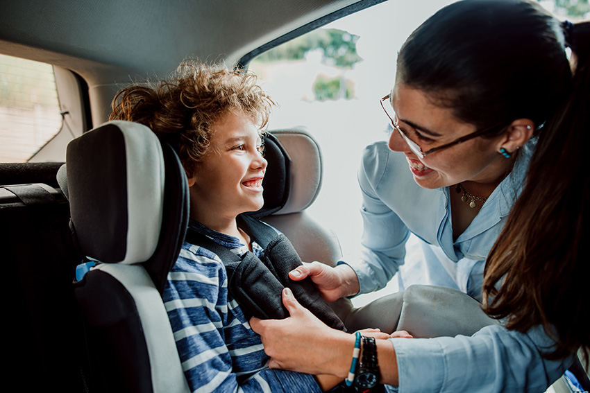 Woman checks child's car seat is fitted properly for safety measures so child can avoid injury in case of a accident.
