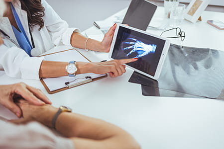 Doctor holding an xray of a hand and pointing out affected areas to the patient
